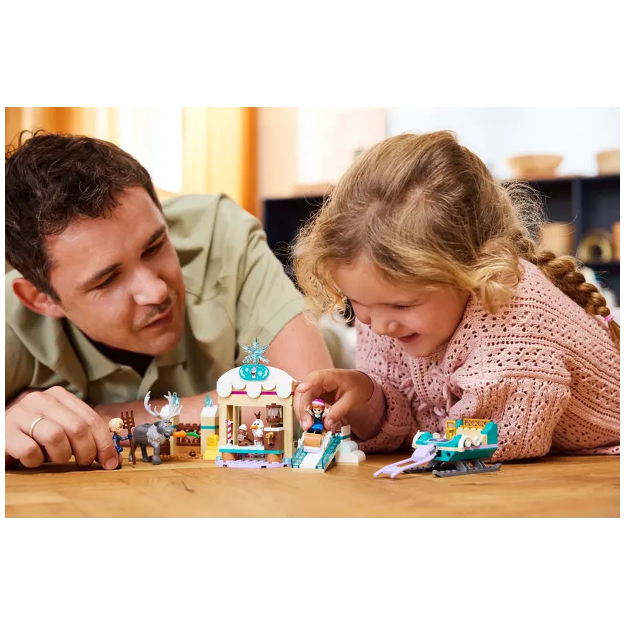 Father and daughter play together on the floor, focusing on LEGO Disney Frozen Anna's Sleigh Adventure set features Anna and Olaf with a sleigh and hot chocolate stand.