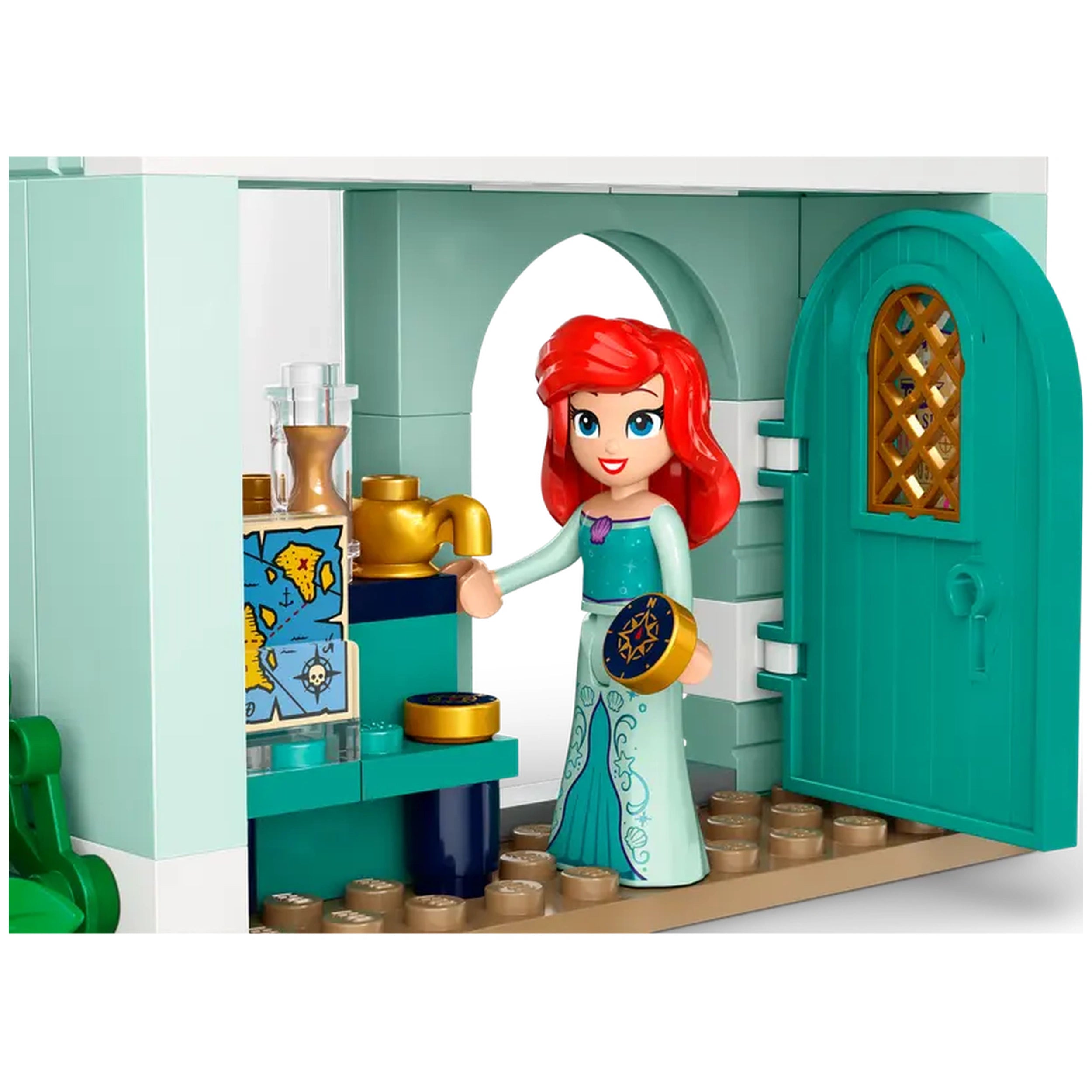 A LEGO® Disney Princess set featuring a smiling character with red hair, wearing a teal top and sparkly skirt, standing beside a colorful countertop with decorative items and an open turquoise door.