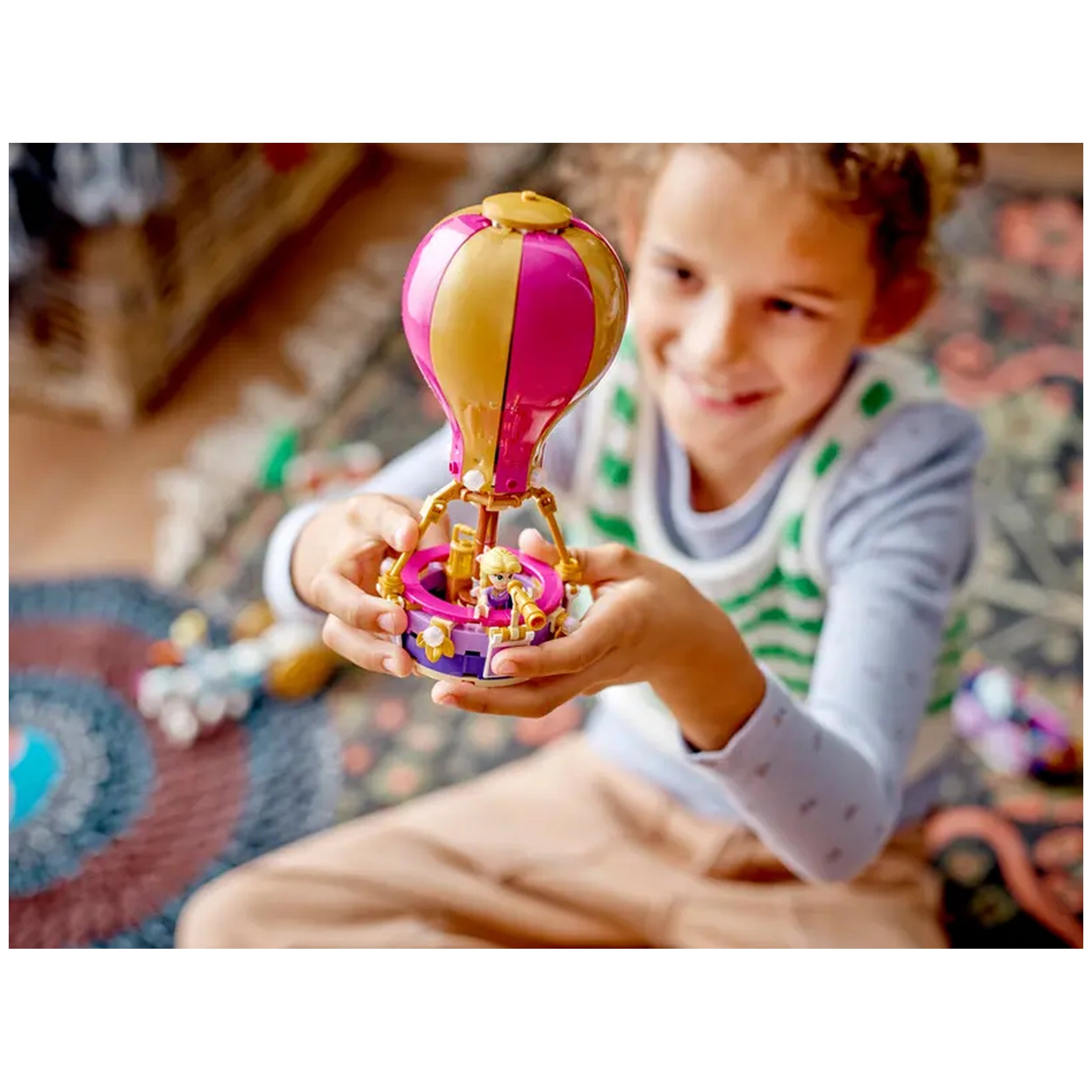 A child smiles while holding a colorful LEGO® Disney Princess hot-air balloon, with a mini-doll seated inside.