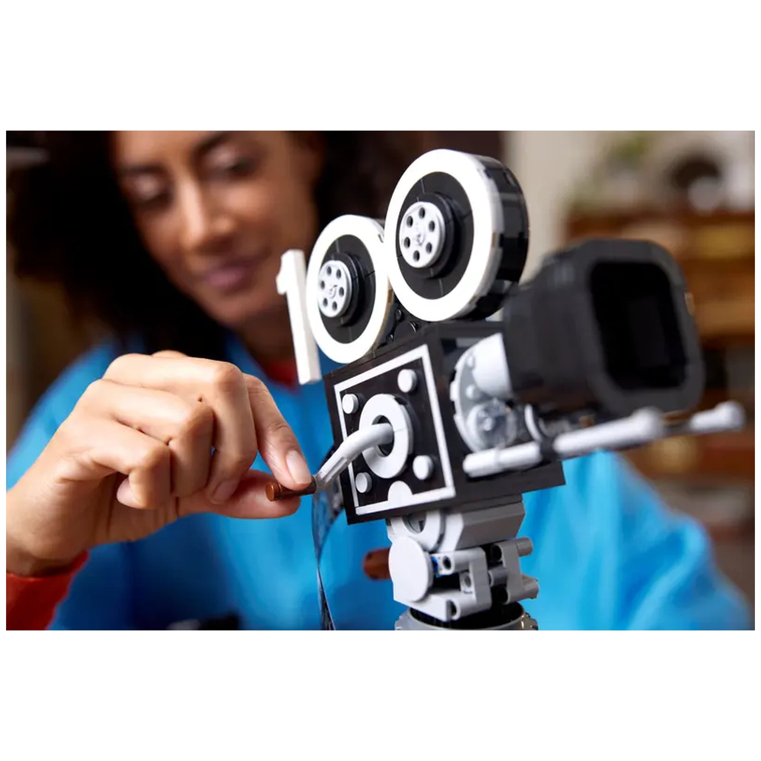 A person adjusts a vintage-style LEGO® movie camera with black and white wheels, focusing on details like the film strip and clapperboard.
