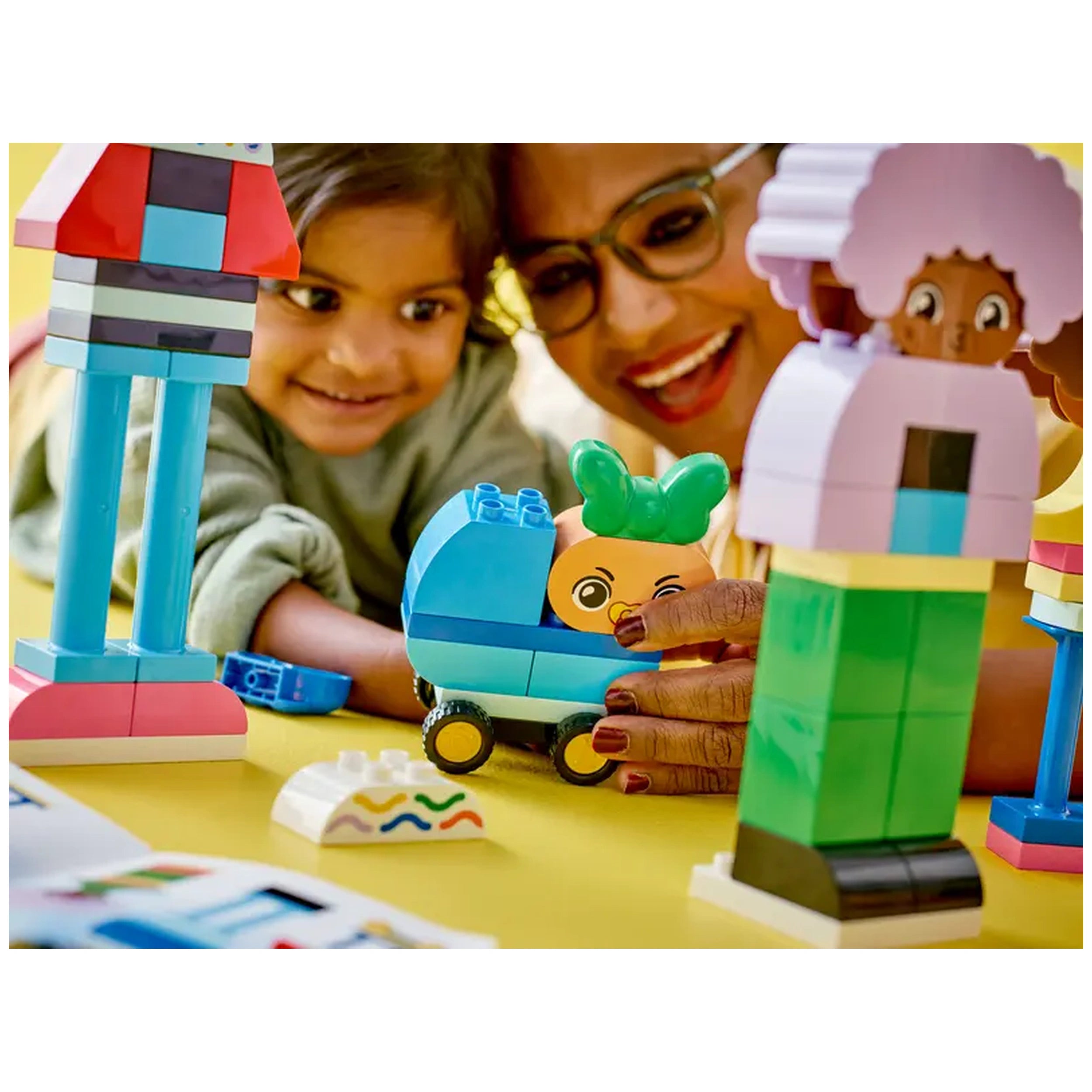 A smiling child and an adult interact with colorful LEGO® DUPLO® characters and a playful vehicle on a yellow surface.
