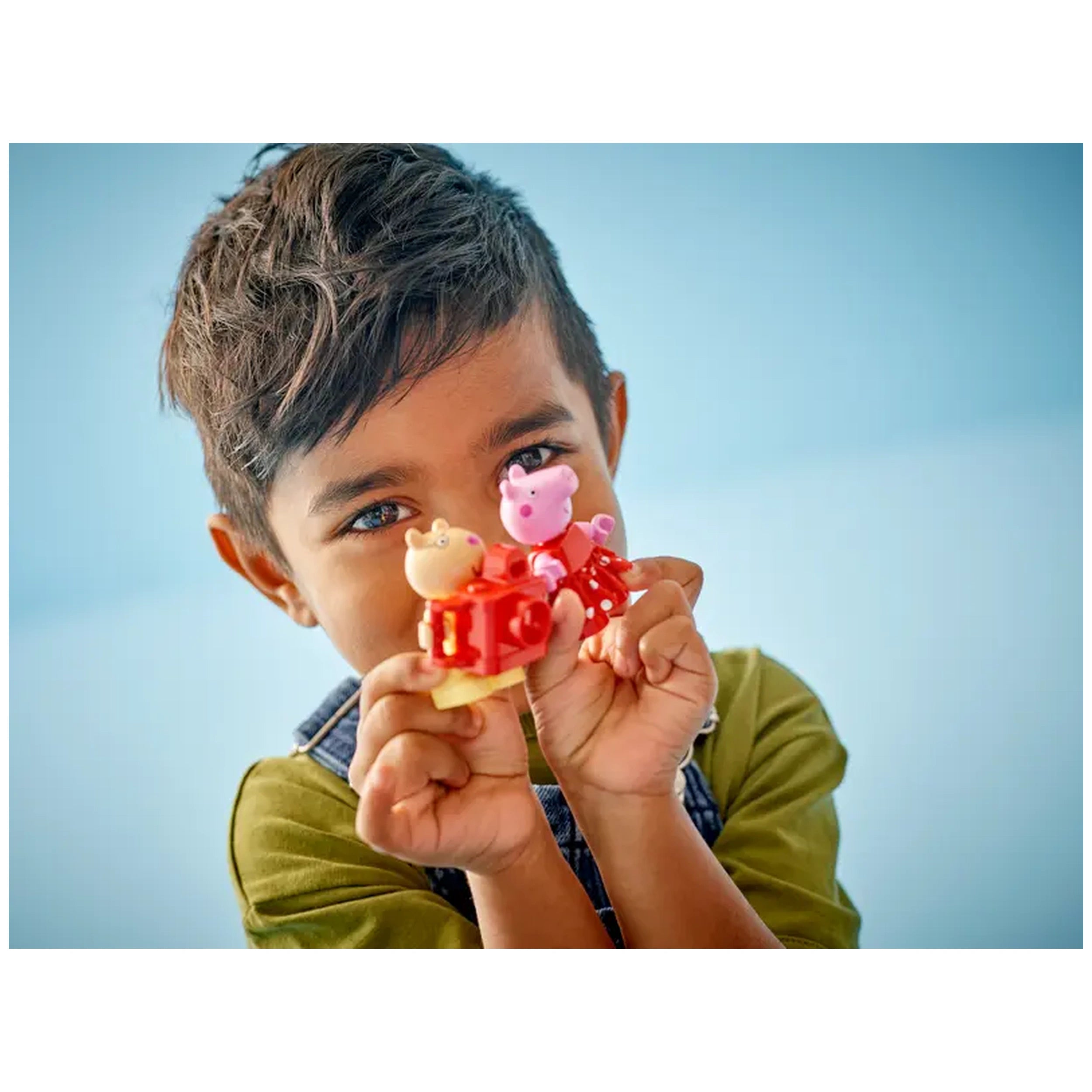 A smiling child holds colorful Peppa Pig toy figures, showcasing a joyous expression against a soft blue background.
