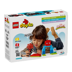A young child lies on their stomach, focused on playing with the LEGO® DUPLO® Spin’s Motorcycle Adventure set, featuring a black motorcycle, Spider-Man figure, and colorful building elements. The child is engaged, stimulating their creativity and fine motor skills. The vibrant packaging showcases the set's educational benefits and connection to Spidey and His Amazing Friends.