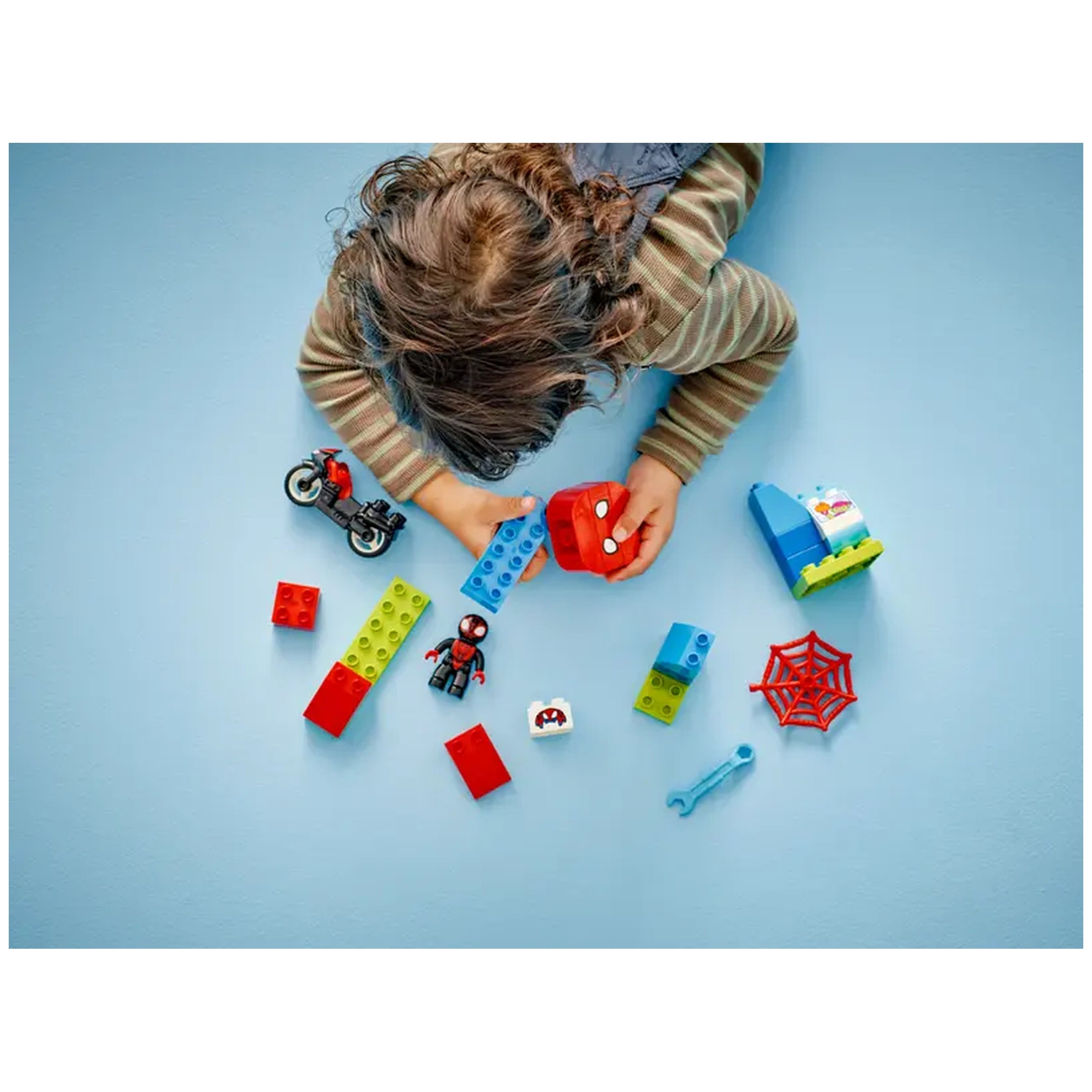 A child plays with colorful LEGO® DUPLO® pieces, including a Spider-Man figure, a motorcycle, and building blocks in green, red, and blue.