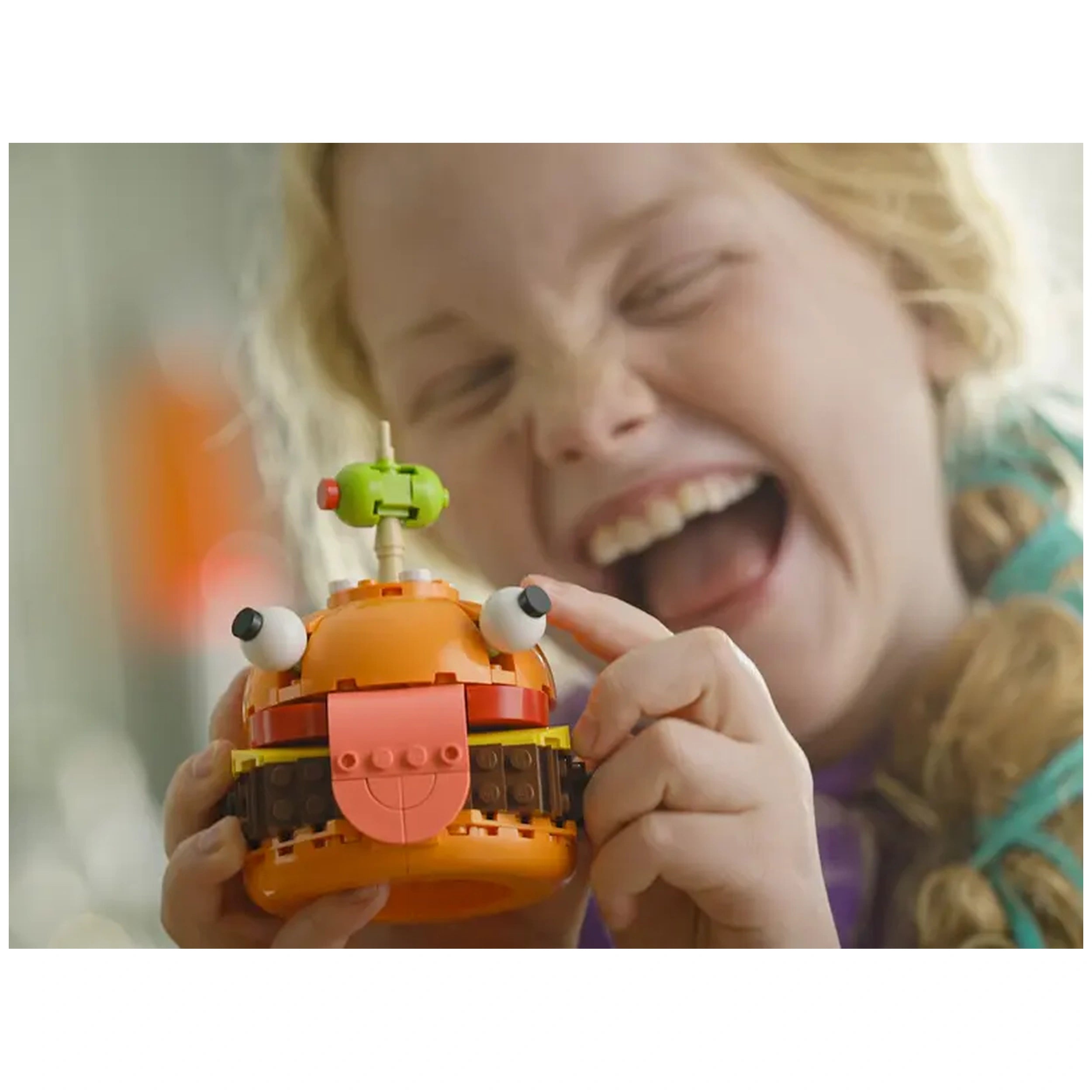 A joyful child holds a brightly colored LEGO® Durrr Burger model with expressive eyes and a playful tongue, laughing excitedly.