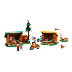 LEGO Friends Adventure Camp set featuring two colorful cabins, a tree, and three mini-dolls engaged in camping activities.
