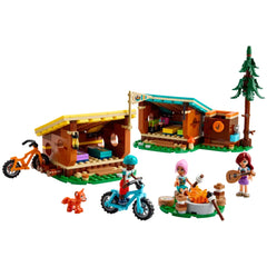 LEGO Friends Adventure Camp Cozy Cabins set featuring two colorful cabins, three mini-dolls, a fox, mountain bikes, and a campfire scene.