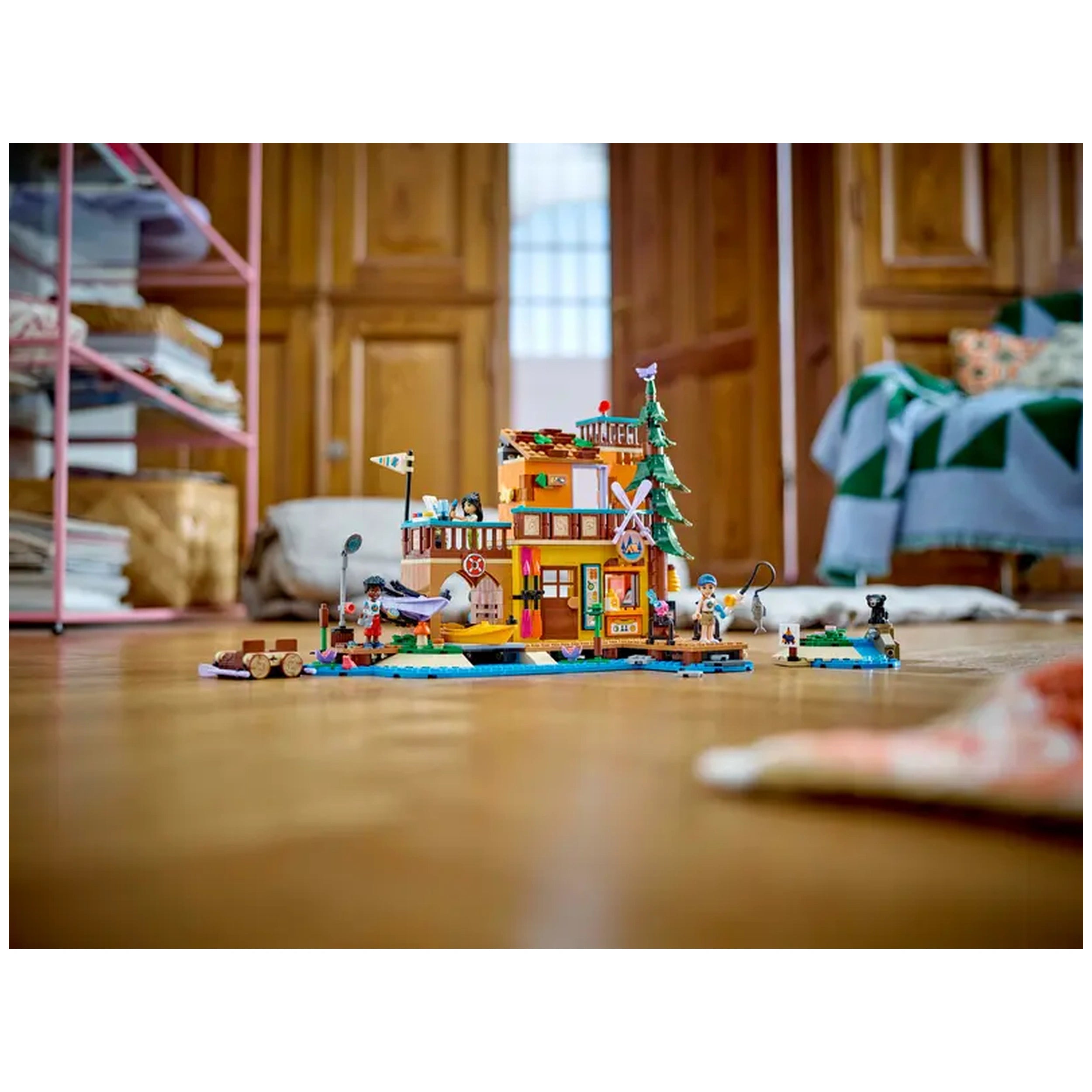 Colorful LEGO Friends Adventure Camp Water Sports set showcasing a multi-level camp building, characters engaging in water activities, and scenic accessories, all on a wooden floor.