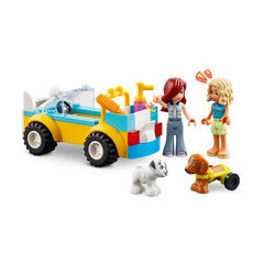 Two mini-dolls, one with red hair and the other with blonde hair, play beside a colorful LEGO® Dog-Grooming Car. The car features a blue and yellow design and is equipped with pet grooming accessories. Two miniature dogs, one white and one brown, sit on the ground as the girls interact with them in a lively pet care scene.