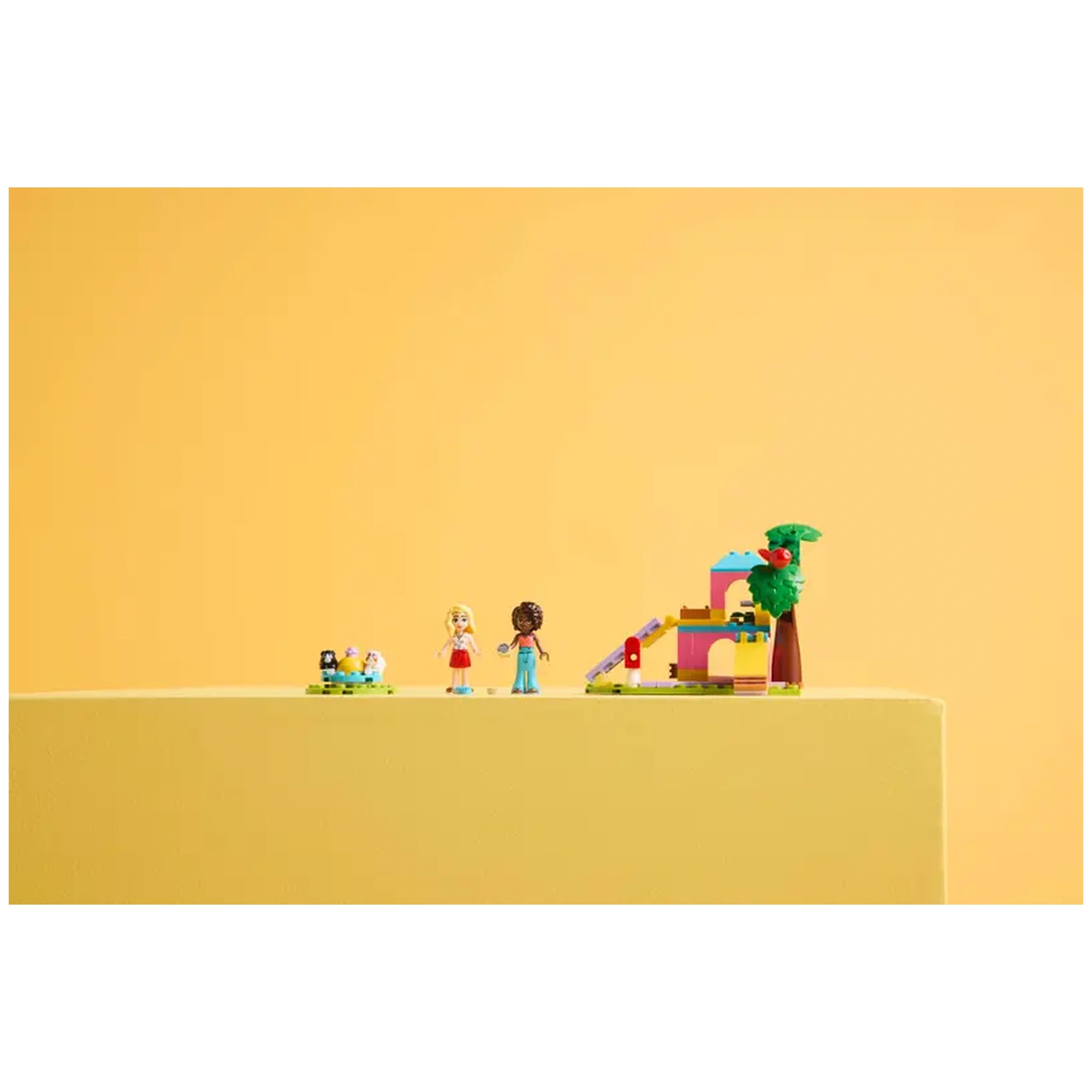 LEGO Friends Guinea Pig Playground set featuring two minidolls and two guinea pigs, with colorful play structures and a tree against a bright yellow backdrop.