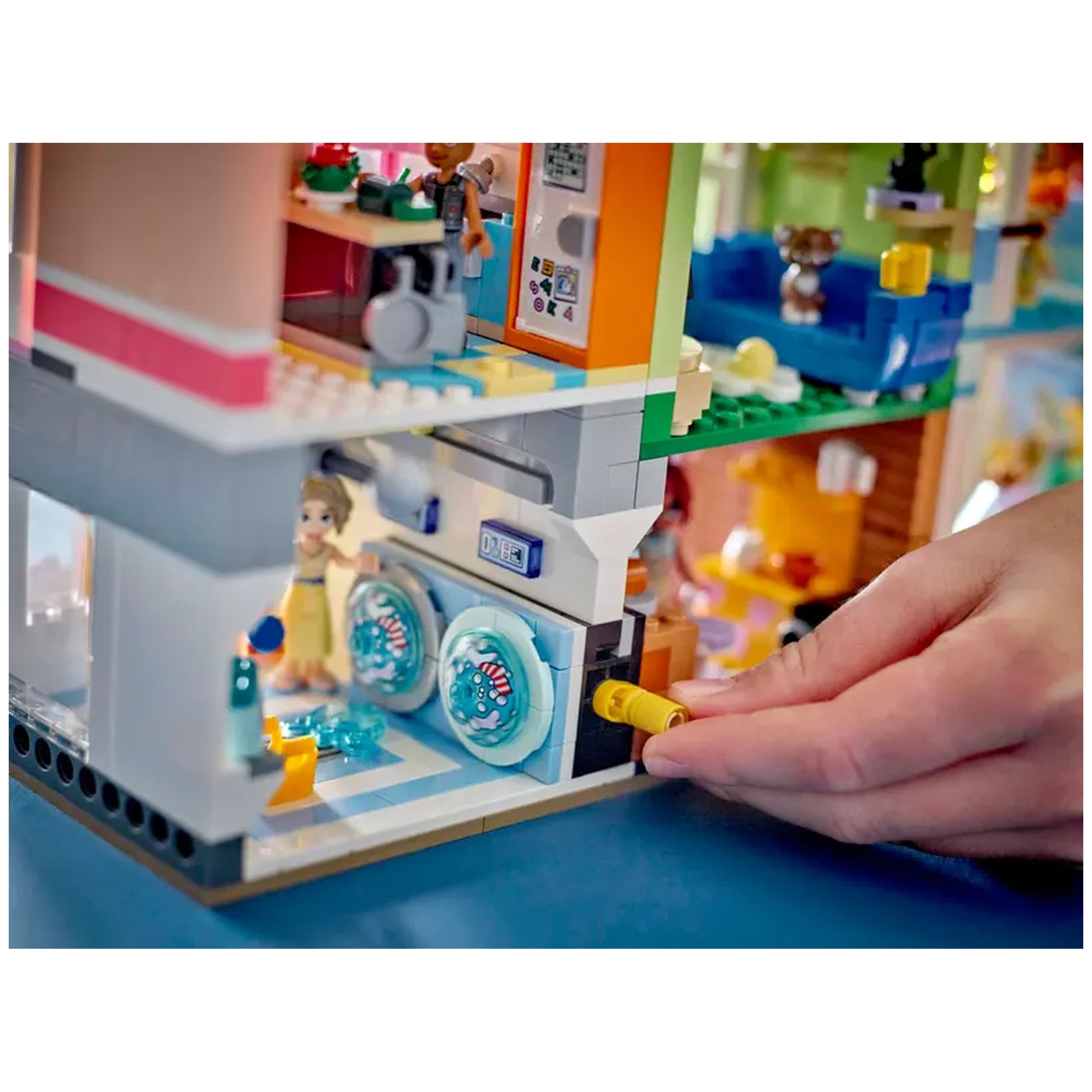 A colorful LEGO Friends set featuring a detailed laundry room, complete with two blue washing machines. A child figure interacts with the machines while decorative accessories enhance the playful scene.