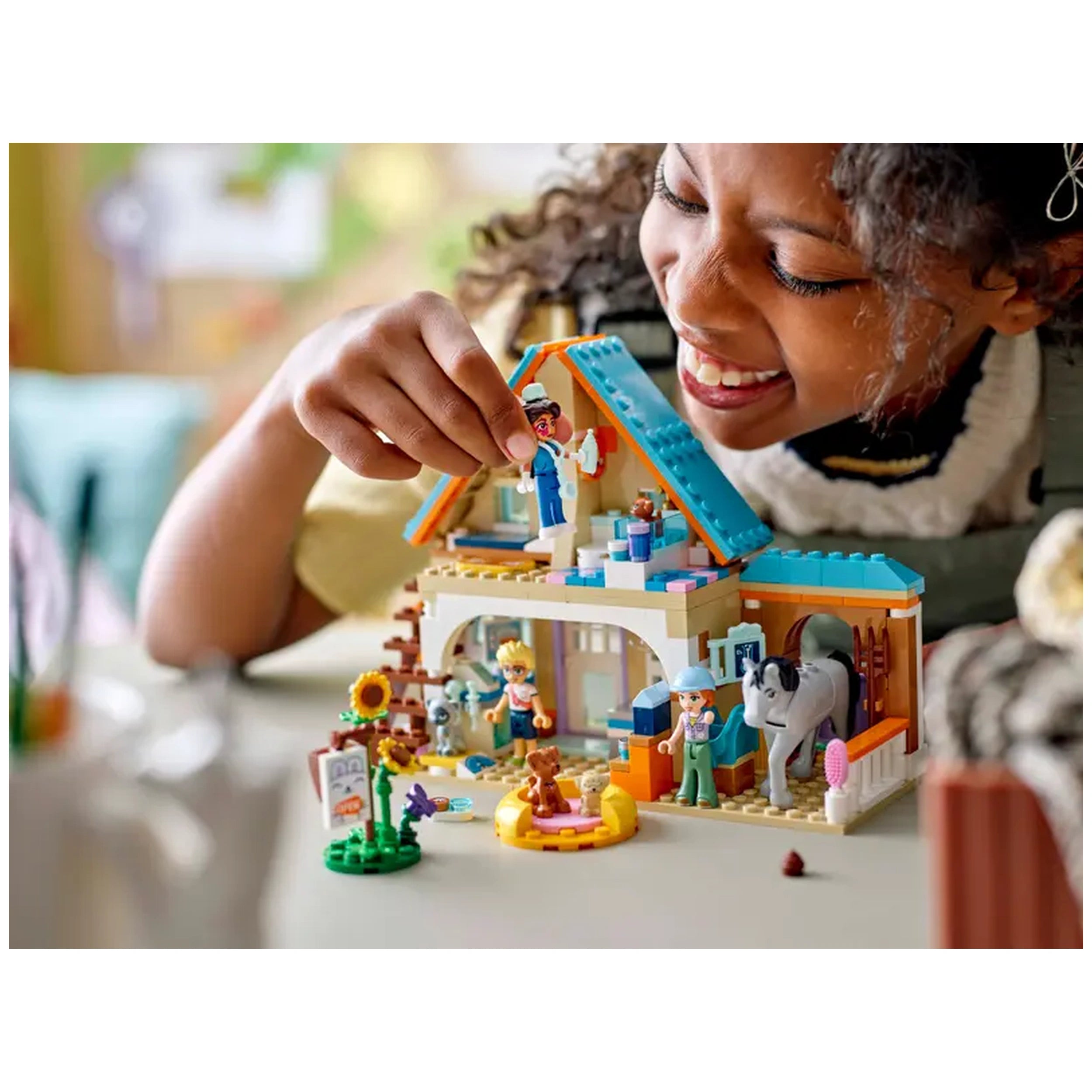 A child joyfully plays with the LEGO® Friends Horse and Pet Vet Clinic set, featuring colorful mini-dolls, a horse, and various pet figures in a vibrant outdoor setting.