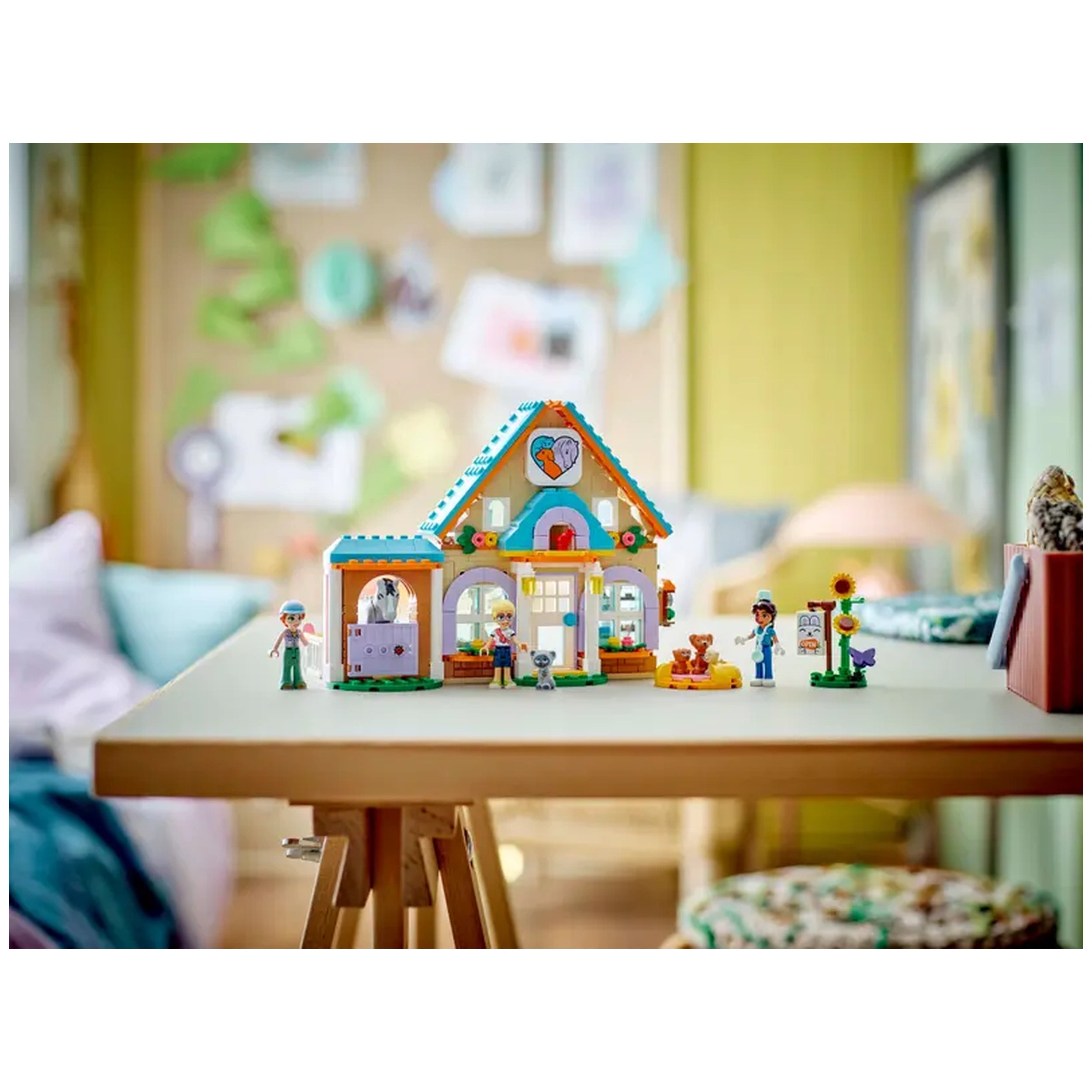Colorful LEGO Friends Horse and Pet Vet Clinic set with three minidolls, a horse, dogs, and a cat, placed on a wooden table in a cozy room.