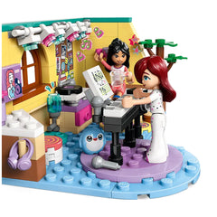 Two LEGO Friends minidolls, one with dark hair and the other with red hair, engage in a playful music session at a colorful room. The scene includes a piano, a cute blue bunny figure, and vibrant music-themed decor on the walls, highlighting creativity and friendship.
