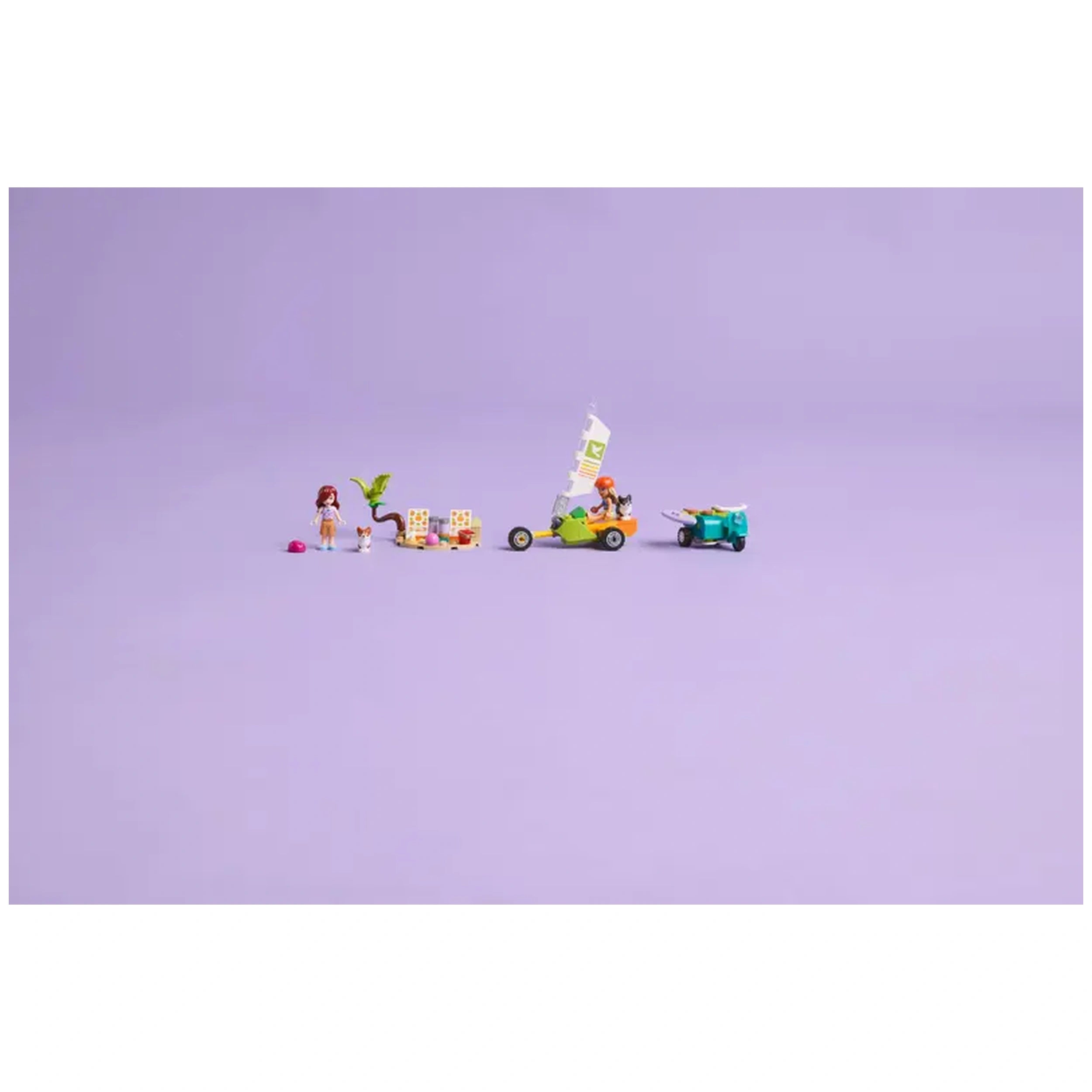 Two LEGO Friends minidolls with vibrant outfits stand beside playful elements, including a green go-kart, a palm tree, and two corgis on a soft purple background.