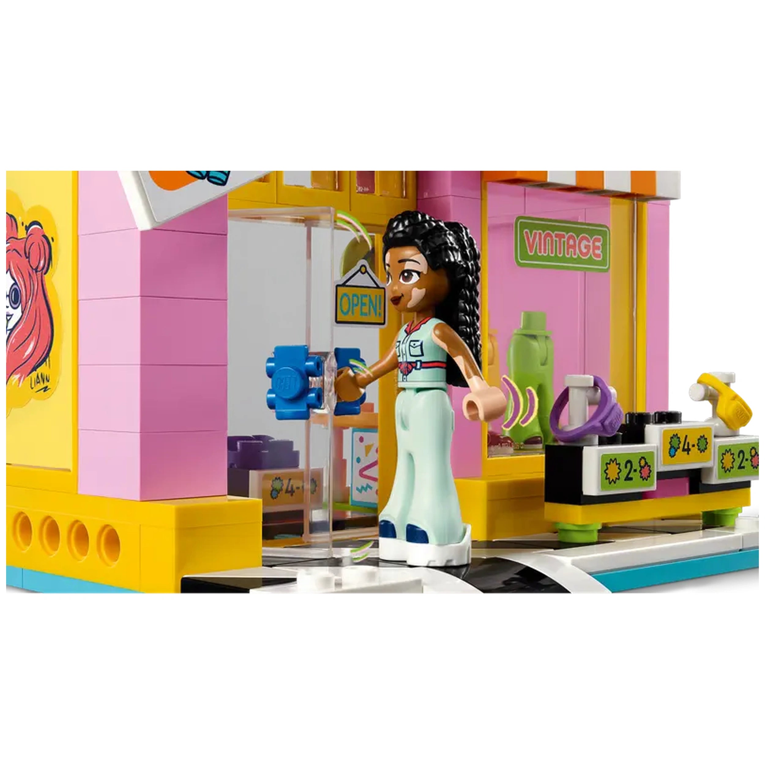 LEGO Friends Vintage Fashion Store with a character in stylish attire, standing at the open door, ready for customers. Colorful shopfront with "OPEN" sign and various accessories displayed.