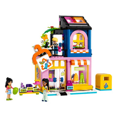 LEGO Friends Vintage Fashion Store set featuring three characters, a cat, and bright accessories. The colorful building has a sewing machine and a washing machine for upcycling clothes.