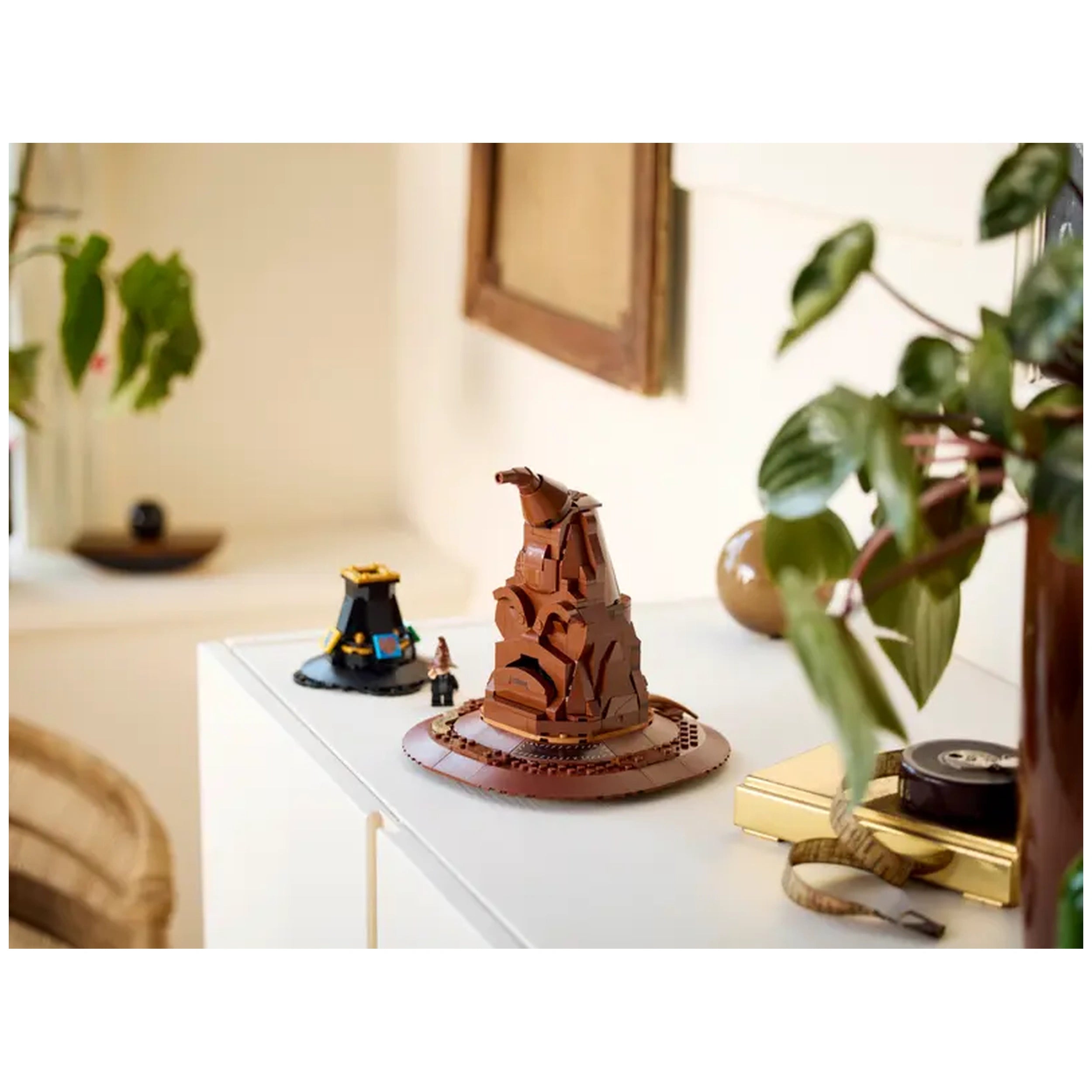 LEGO Harry Potter Talking Sorting Hat construction set displayed on a white table, alongside another small hat and plants in a cozy room.