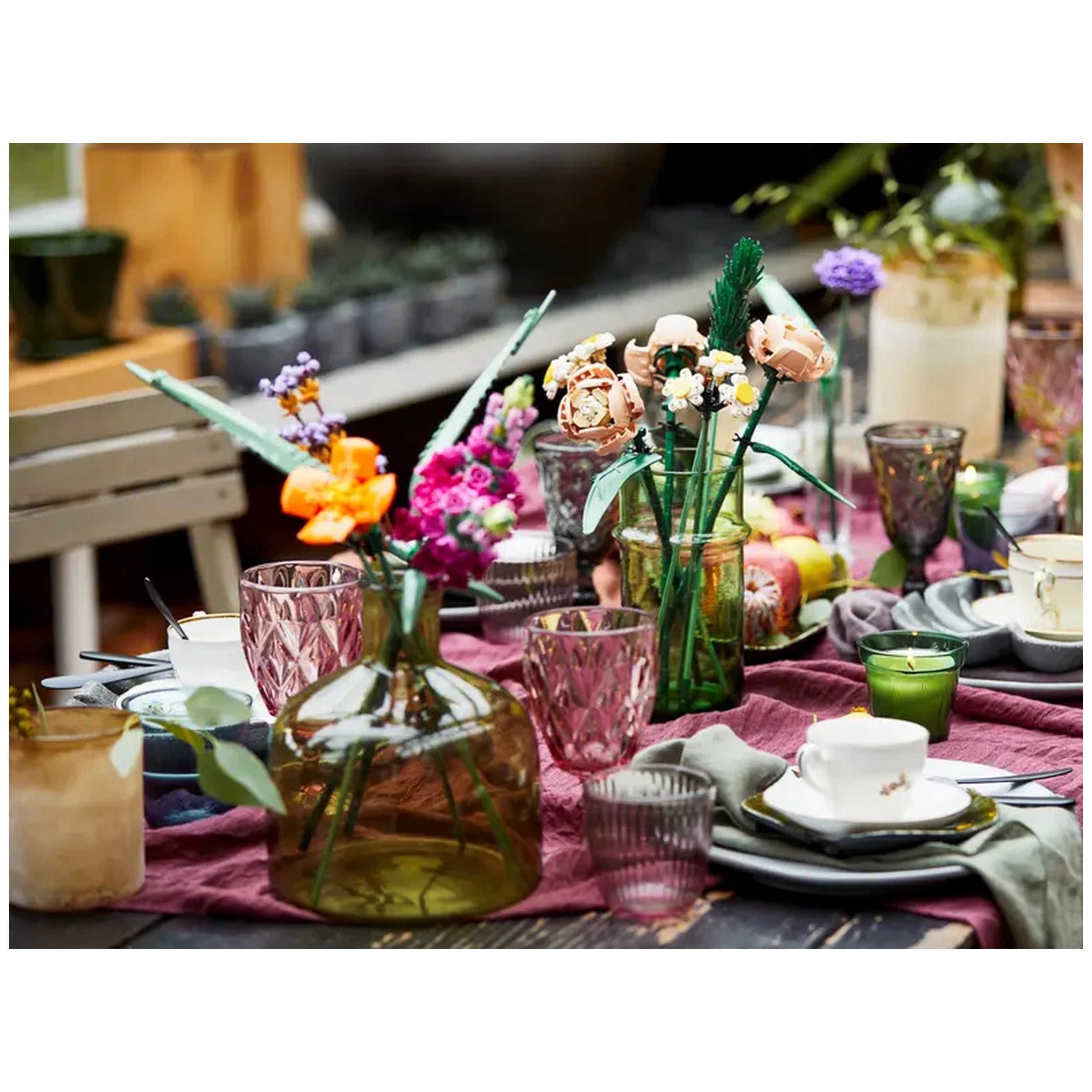 Colorful LEGO flower arrangements in various vases and glasses adorn a dining table covered with a dark purple fabric, showcasing creativity and vibrancy.
