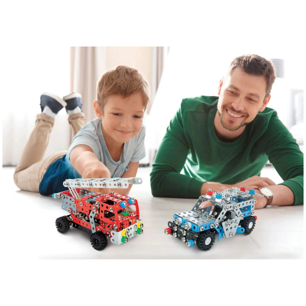Child and adult happily assembling red and blue metal construction toy vehicles on a light-colored floor.