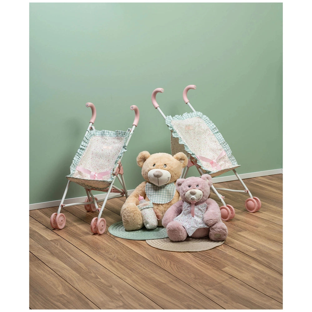 Two teddy bears seated between pink-handled strollers on wooden floor, green wall backdrop.
