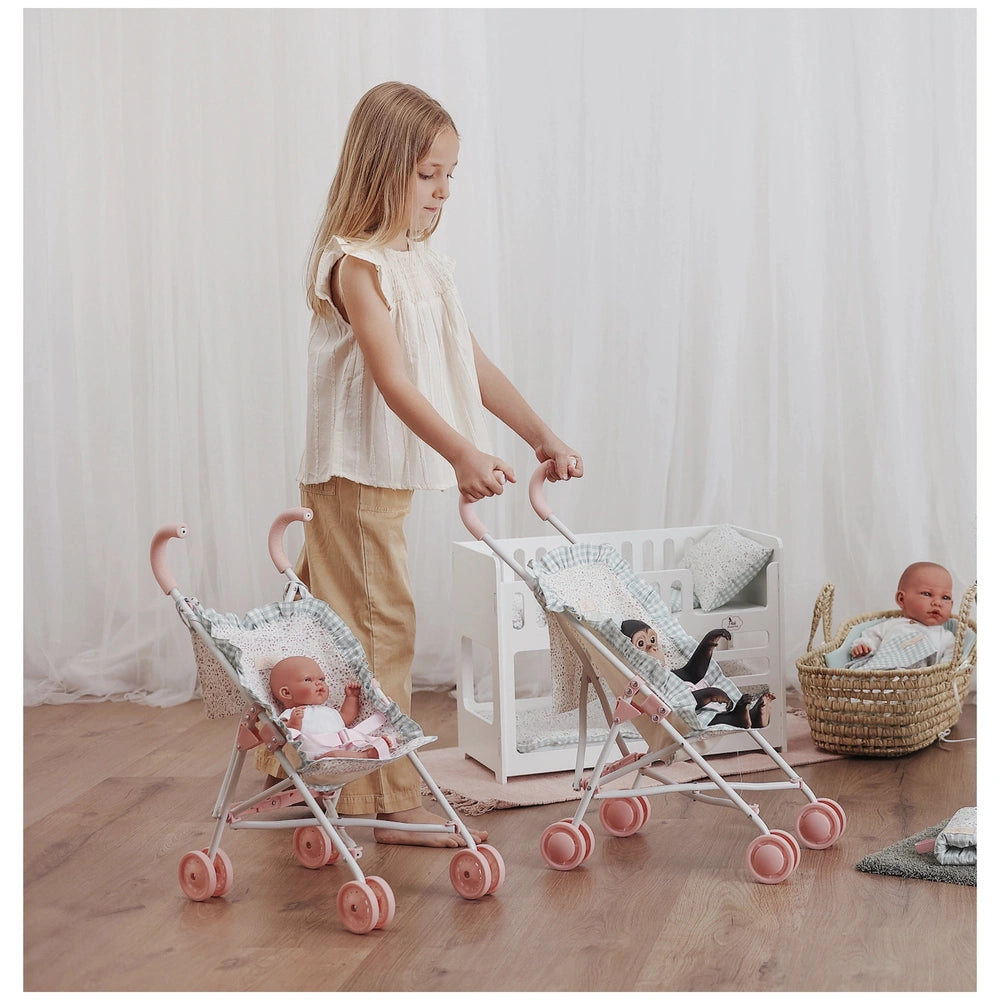 Child playing with pink-handled strollers from ASI Dolls Cloe Collection, each holding a doll, in a softly lit, cozy room.