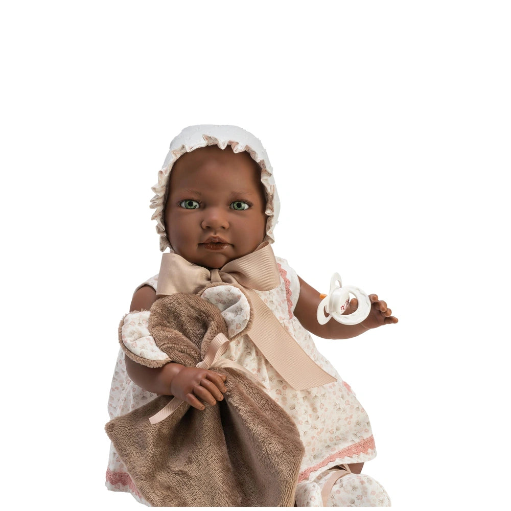 Lara Reborn doll in a floral dress with bonnet, holding a brown blanket and pacifier, seated against a white background.
