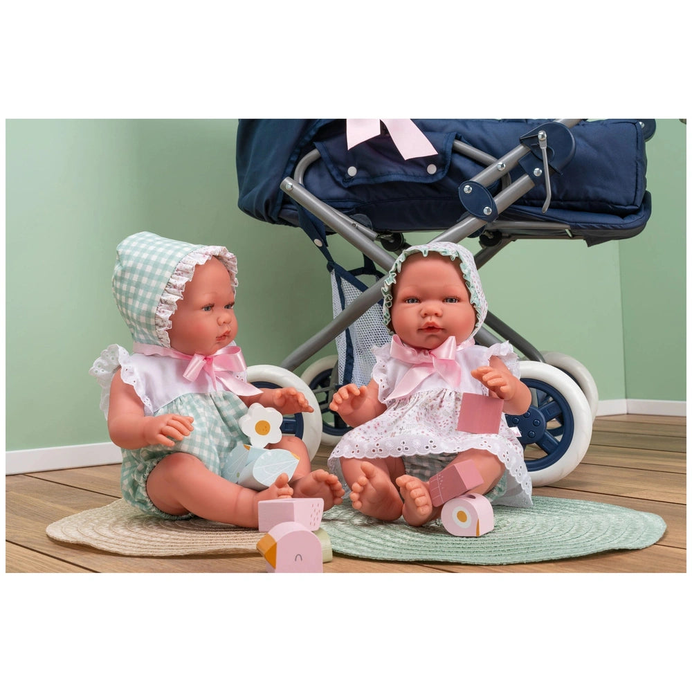 Two Asi Dolls in gingham and lace outfits, sitting on round mats with a toy stroller in the background.
