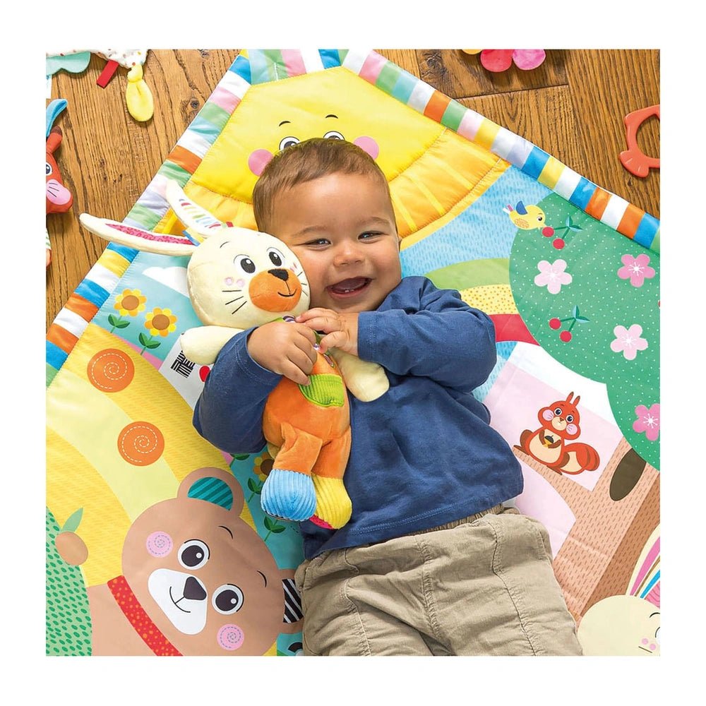 Benny the Puppy stuffed animal is held by a young child on a colorful play mat, surrounded by vibrant patterns.