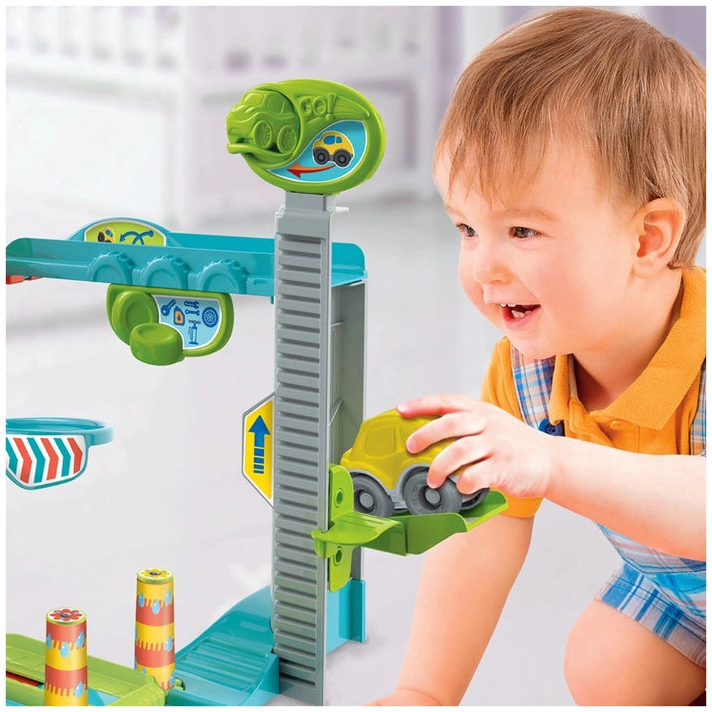 Baby Clementoni Fun Garage toy captivates a smiling toddler in a yellow shirt and blue shorts, promoting tactile play.