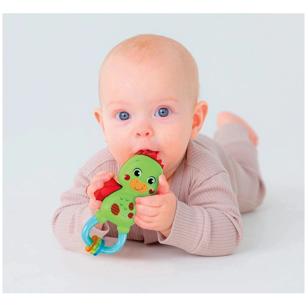 Baby Clementoni Little Dragon Rattle in a young child's hands, with the baby lying on a white surface and looking playfully a