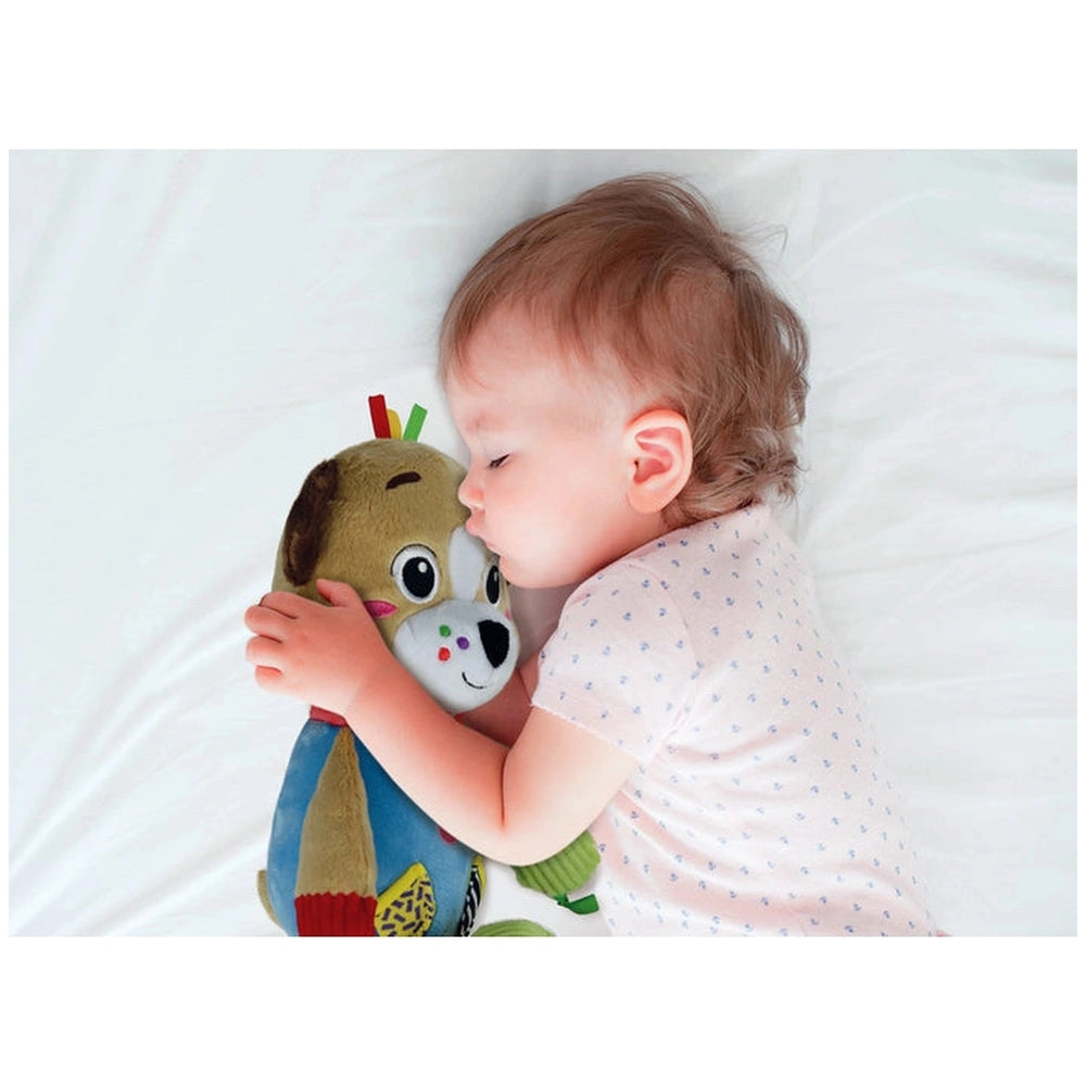 Baby Clementoni's Pete The Puppy stuffed animal is held by a peacefully sleeping child on a soft white surface.