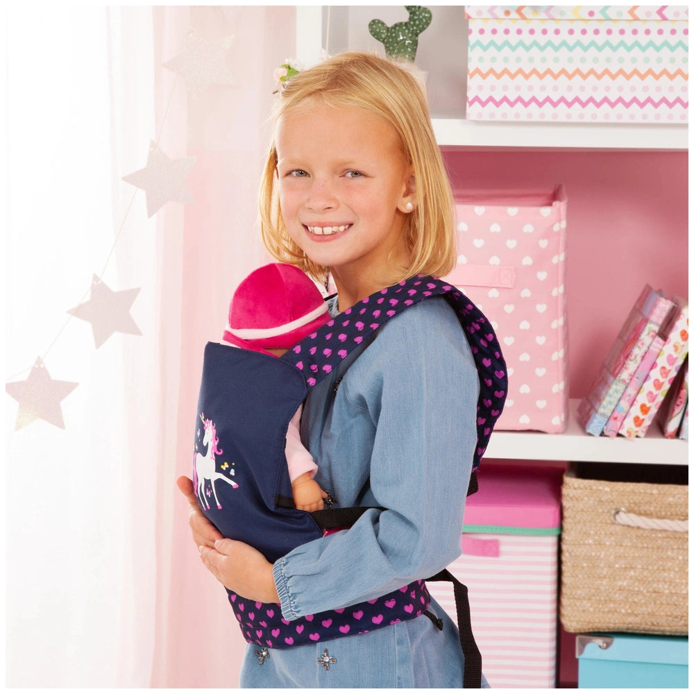 BAYER DESIGN unicorn doll carrier in blue and pink held by a young girl with blonde hair, surrounded by pink decor.