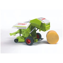 Green and white toy Claas Rollant 250 Straw Baler with red wheels, next to a rolled straw bale.