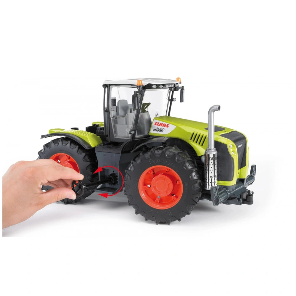 Hand turning the steering wheel of a 1:16 scale Bruder Claas Xerion 5000 toy tractor, featuring a green exterior and large red wheels.