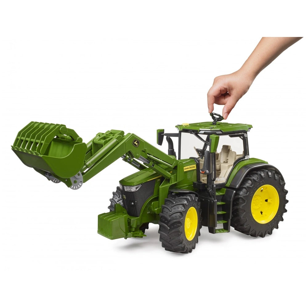 Hand operating Bruder John Deere 7R 350 toy tractor with frontloader. Green body, yellow wheels, realistic design.