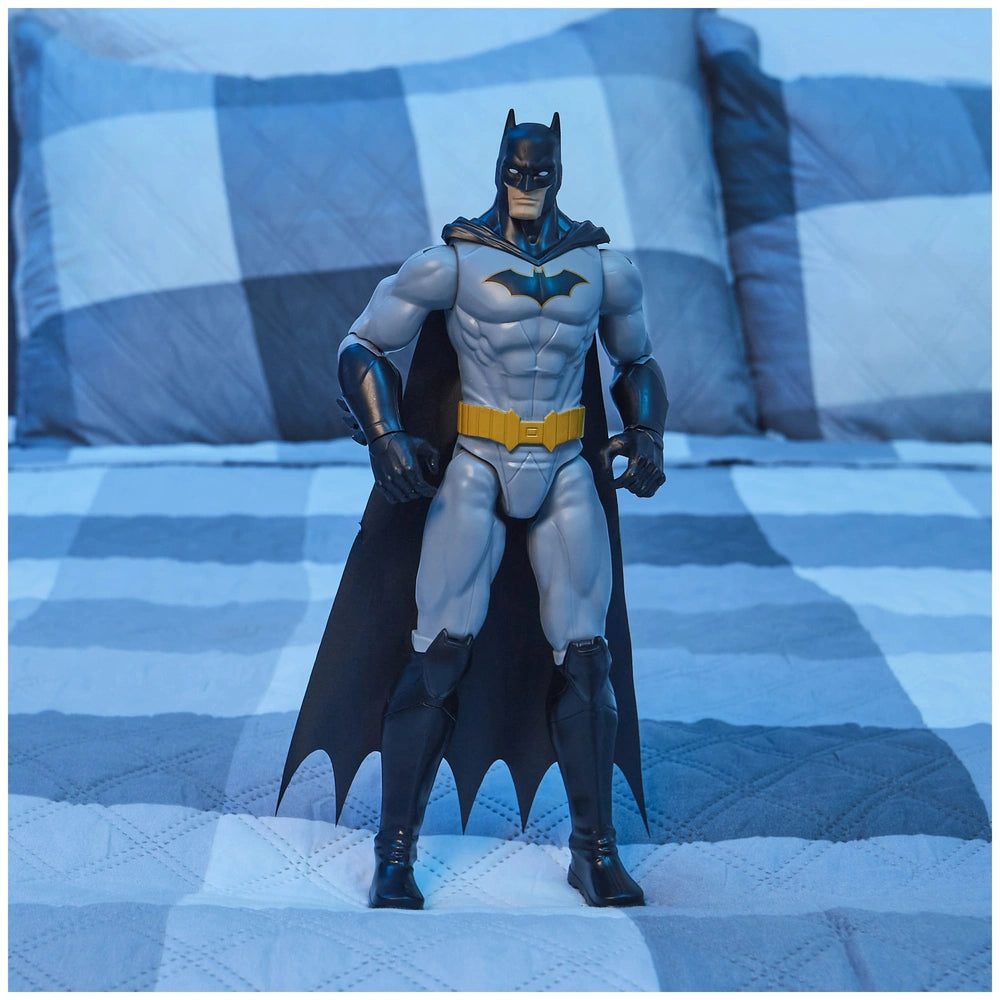 Batman action figure in black and yellow stands on a blue and white checkered bedspread, showcasing detailed muscular feature