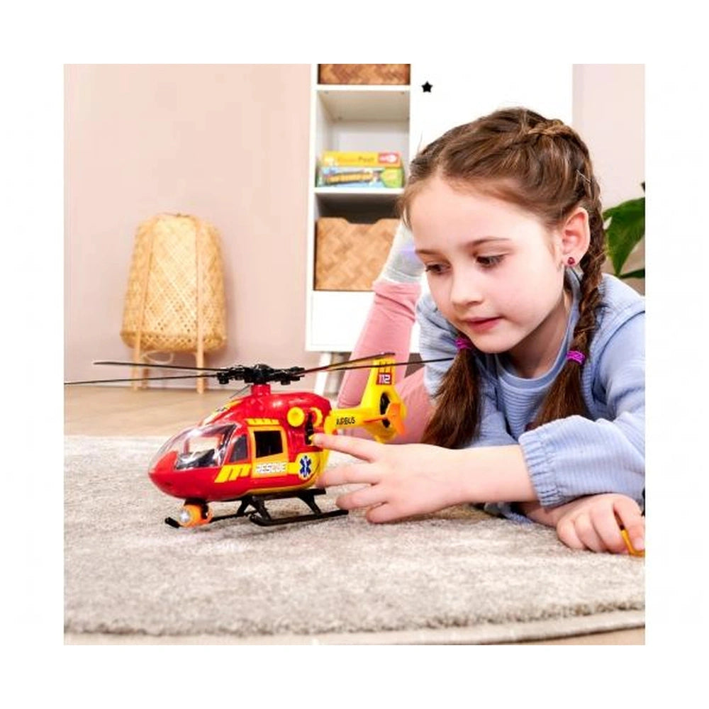 Dickie ambulance helicopter Airbus H145 in red and yellow, played with by a young girl in a blue shirt on a gray carpet.