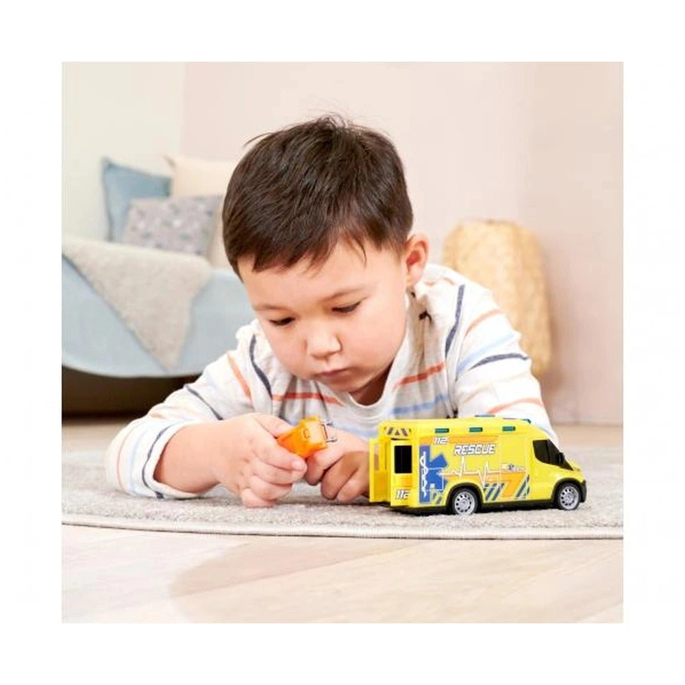 Young child playing with a yellow plastic Iveco Daily ambulance toy in front of a fabric couch with pillows.