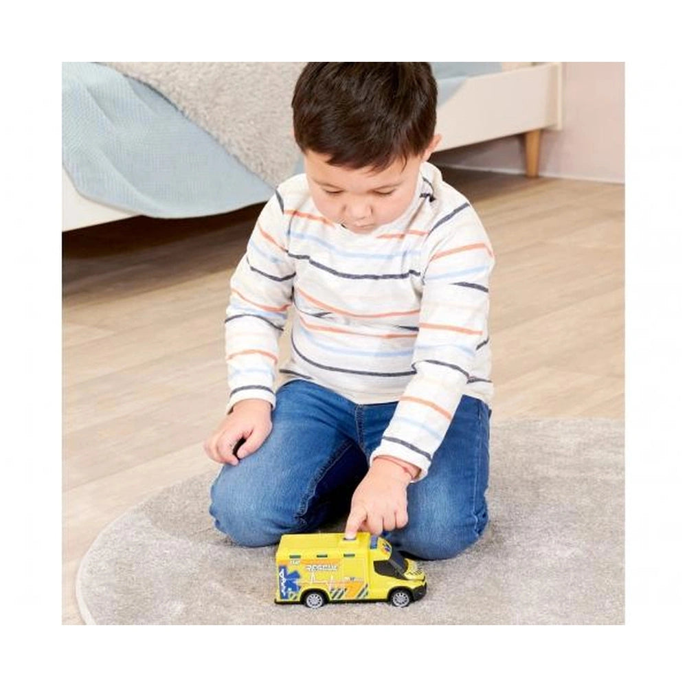 Young child in striped shirt and blue jeans plays with yellow Iveco Daily ambulance toy on light carpet.