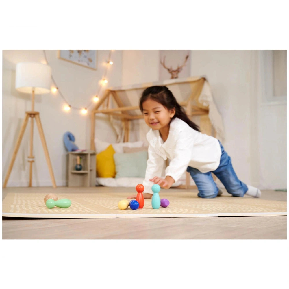Eichhorn bowling game set displayed on a colorful rug as a young girl plays with toys on a wooden floor.
