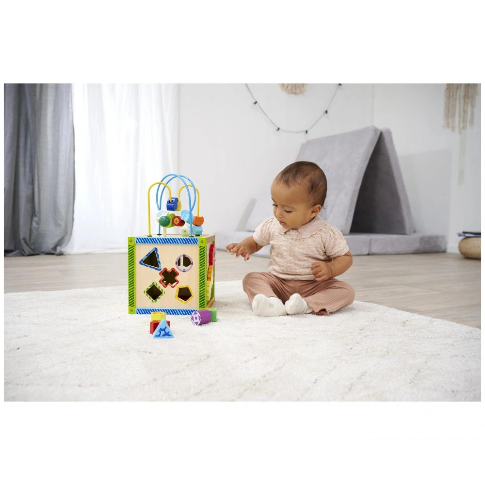Eichhorn Color Little Play Center features a colorful toy box beside a baby sitting on a fluffy white rug indoors.