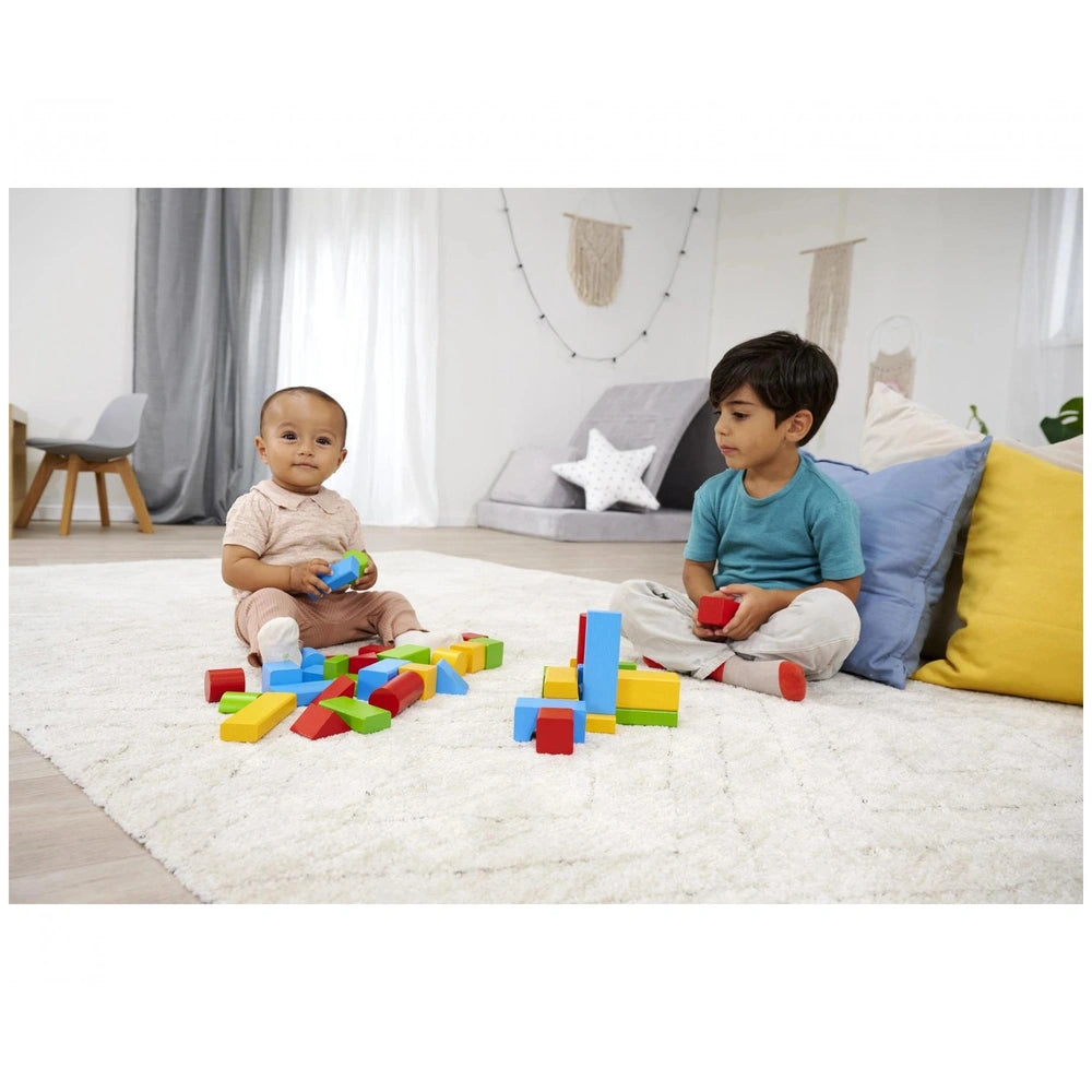 Eichhorn coloured wooden blocks are being enjoyed by two children on a white carpeted floor in a bright indoor setting.