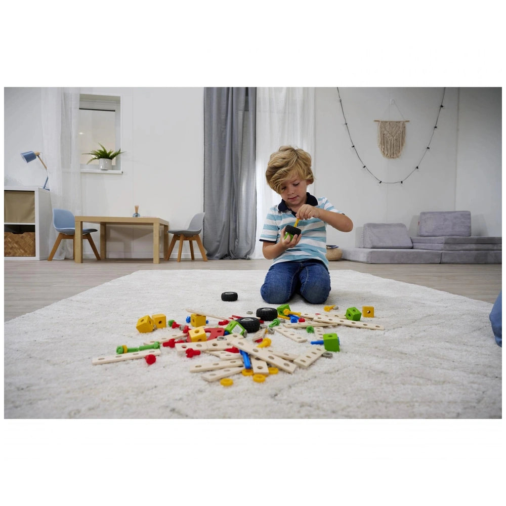 Child playing with Eichhorn construction set toys on a white carpet, surrounded by colorful wooden blocks and plastic pieces.