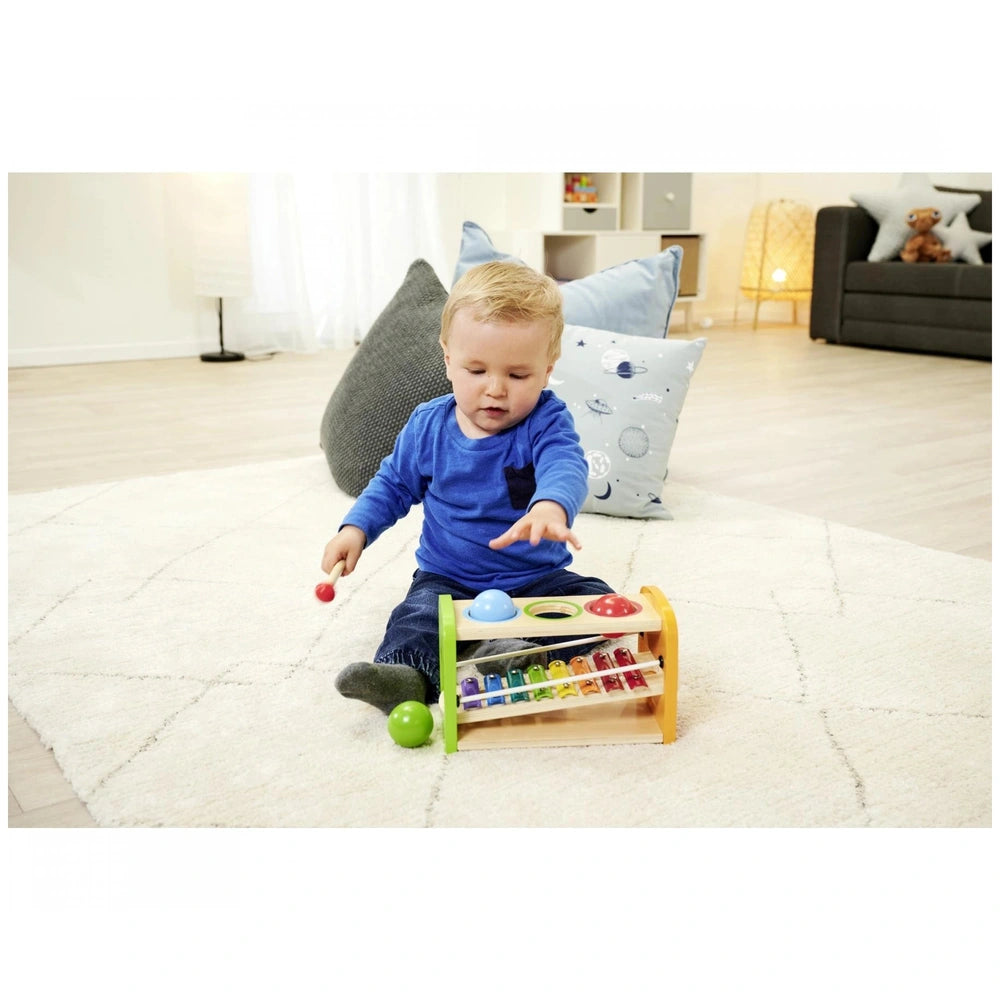Eichhorn Hammer Bench with Xylophone, featuring a child playing with colorful drum pads on a cozy white rug indoors.