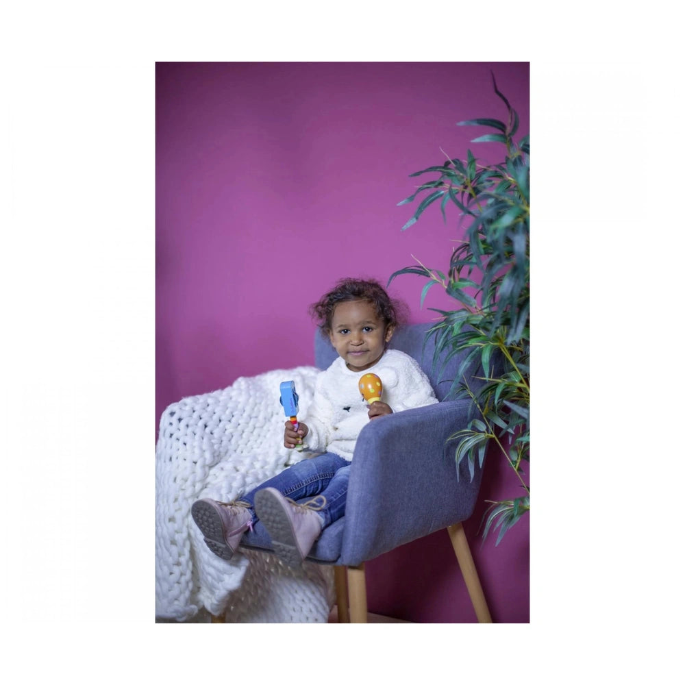 Eichhorn Maracas in a childs hands; cheerful kid in white sweater and blue jeans, smiling with colorful toys.
