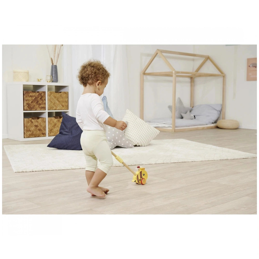 Eichhorn Push Bee toy in a bright room with a child, wooden playhouse, and minimalistic decor featuring natural materials.