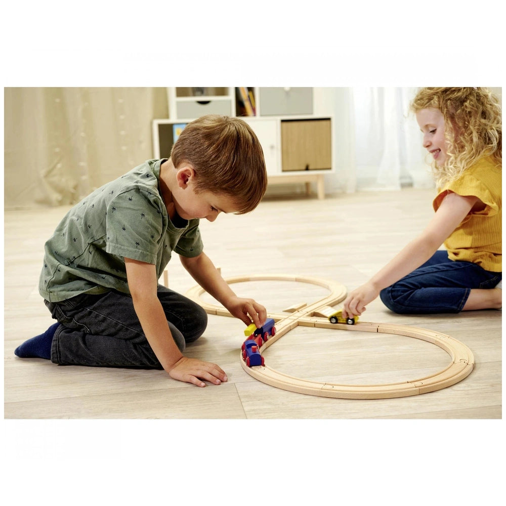 Eichhorn train track playset featured with two children playing on a wooden floor, surrounded by toy trains and bright decor.