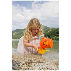 Gowi beach bucket, yellow with monkey face, held by a young girl in a light dress, standing in light blue-green water.