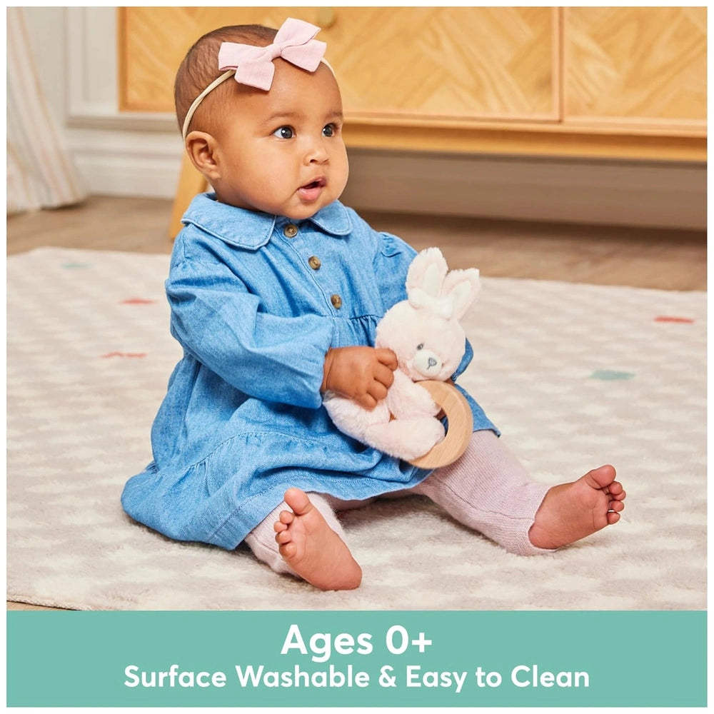 Gund Soft Animal Ring Rattle held by a young child in a blue outfit, sitting on a colorful carpet indoors.